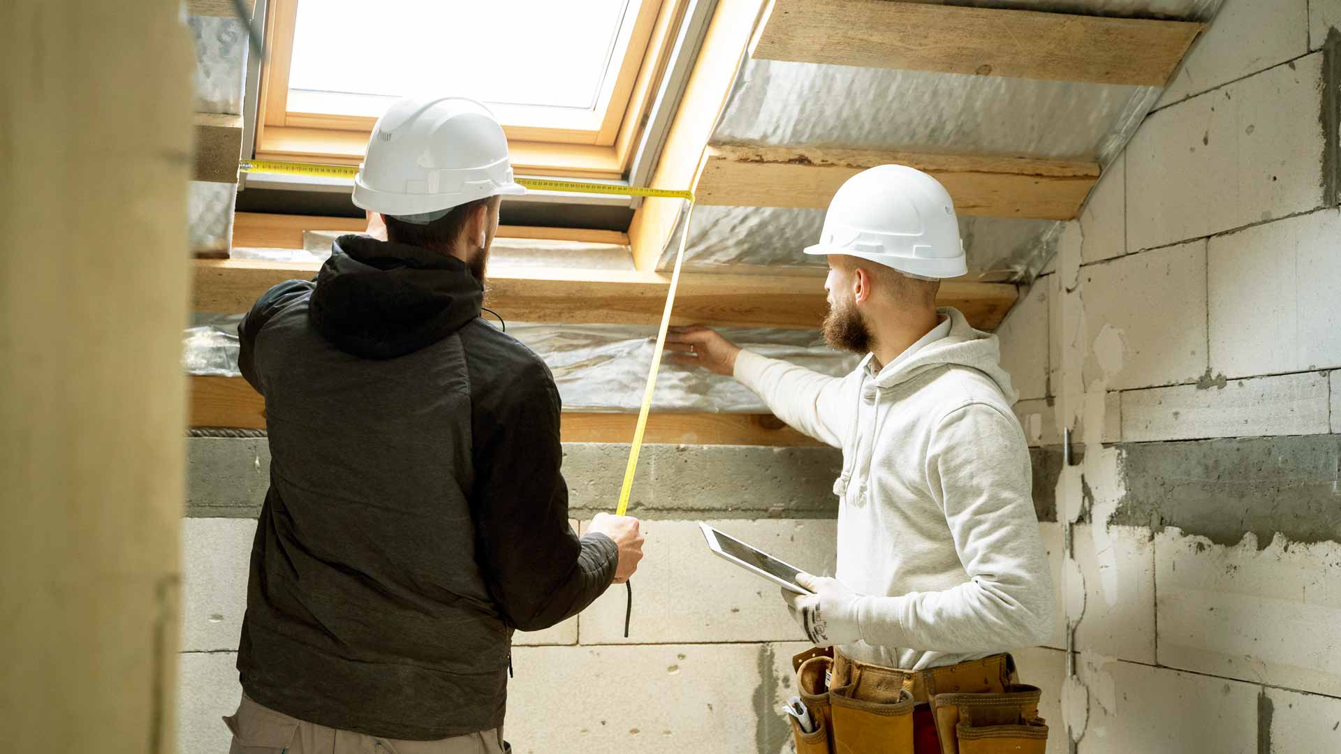 Two people measuring an unfinished roof opening in an attic