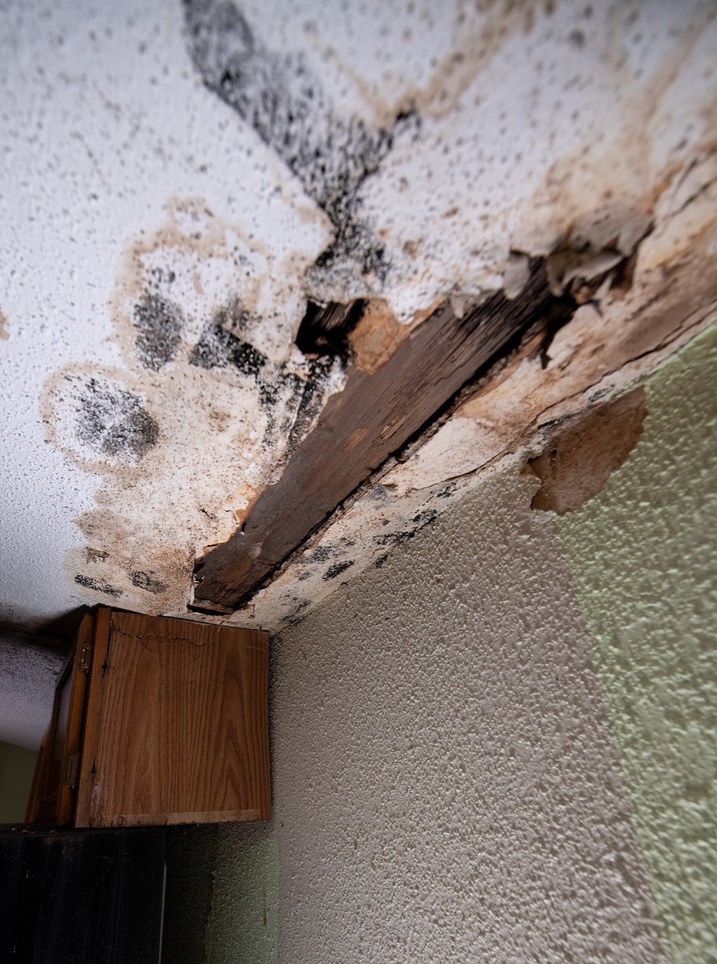 A stained, opened ceiling above kitchen cabinets