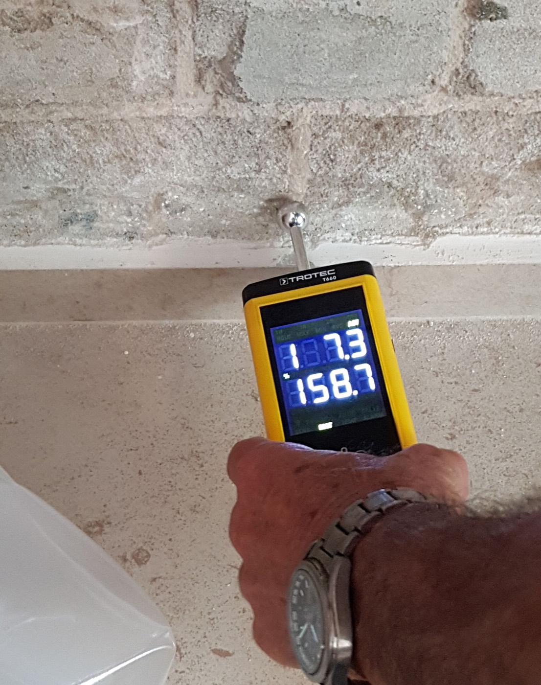 A moisture meter held against a masonry wall